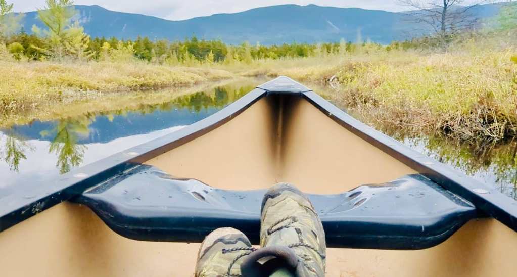 feet stretched out in a canoe with a marshy canal and mountains
